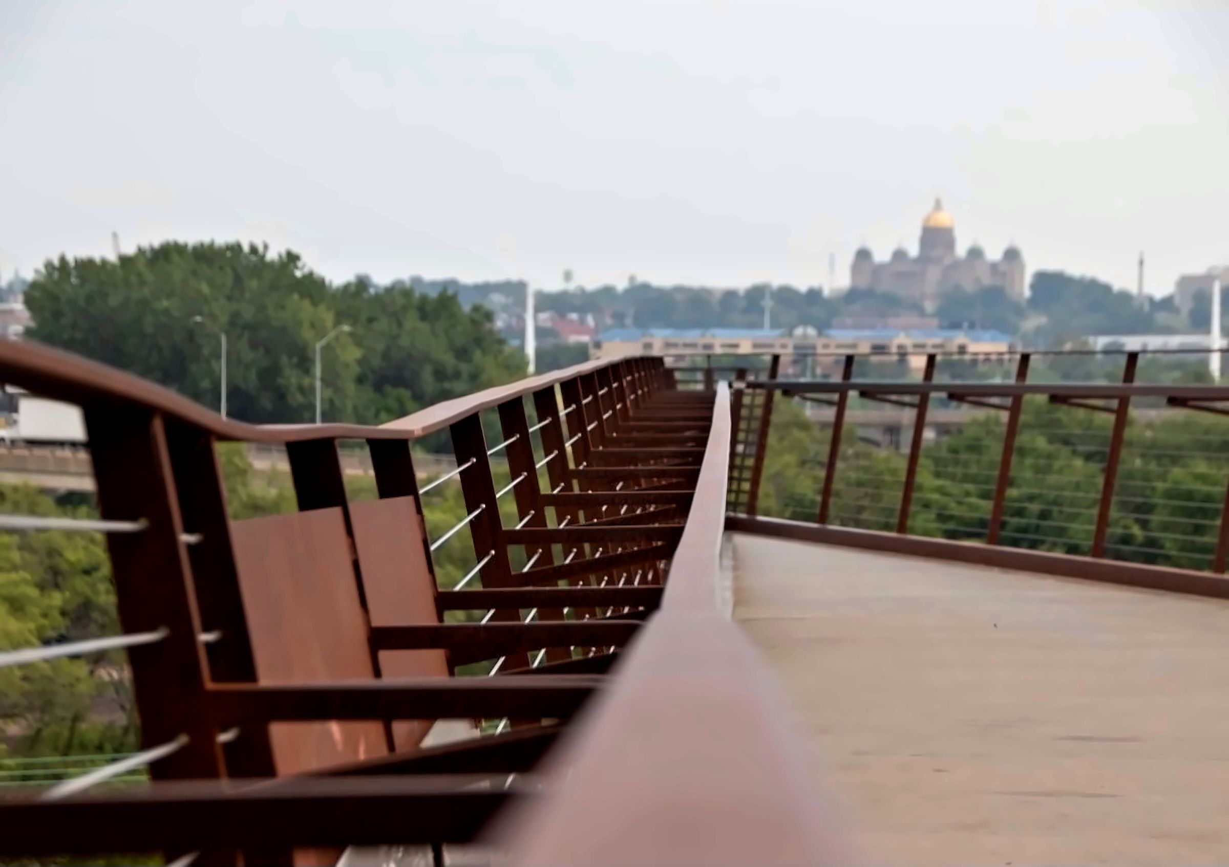 Rusted steel railing of a pedestrian bridge leading toward the Iowa State Capitol